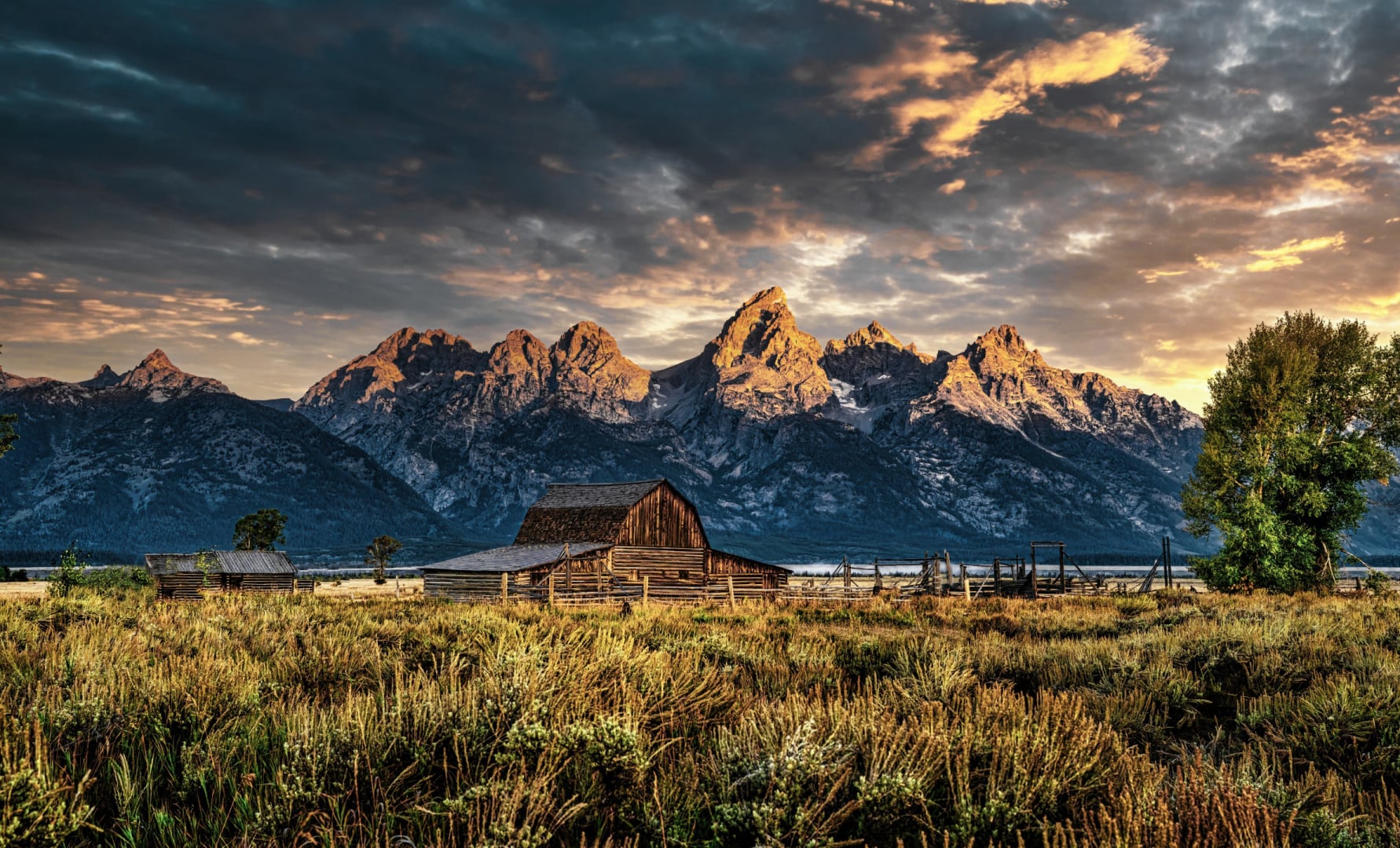 sunrise over the teton mountains behind a weathered barn